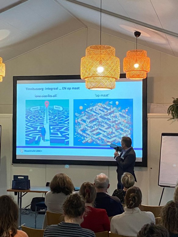 Zaal met mensen en presentatie op een scherm tijdens een ledenbijeenkomst